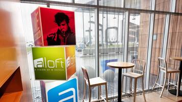 A hotel reception area with a modern design, featuring a glass partition and a display of promotional boxes. There are two round tables and chairs arranged for guests.