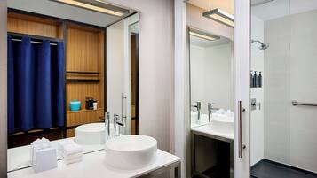 Une salle de bain moderne avec un grand miroir, deux lavabos, une douche et un meuble-lavabo doté d’un porte-serviettes et d’articles de toilette.