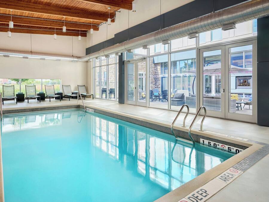 An indoor swimming pool with clear glass walls, a wooden ceiling, and a view of the outside.
