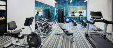 Un gimnasio con diversos equipos de ejercicio, incluyendo cintas de correr, una elíptica y pesas libres.