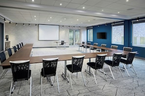 Conference room with a long table, black mesh chairs, and a large screen.