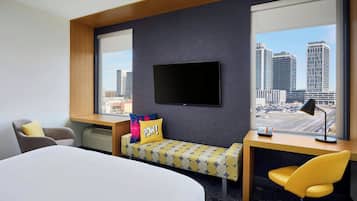 A hotel room with a bed, a desk, a chair, a TV, and a city view.