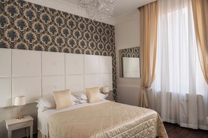 Habitación de hotel con una cama grande, una mesita de noche, un candelabro y un ventanal con cortinas.