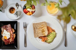 Impostazione per la colazione con pane tostato, salmone affumicato, avocado e una ciotola di frutta.