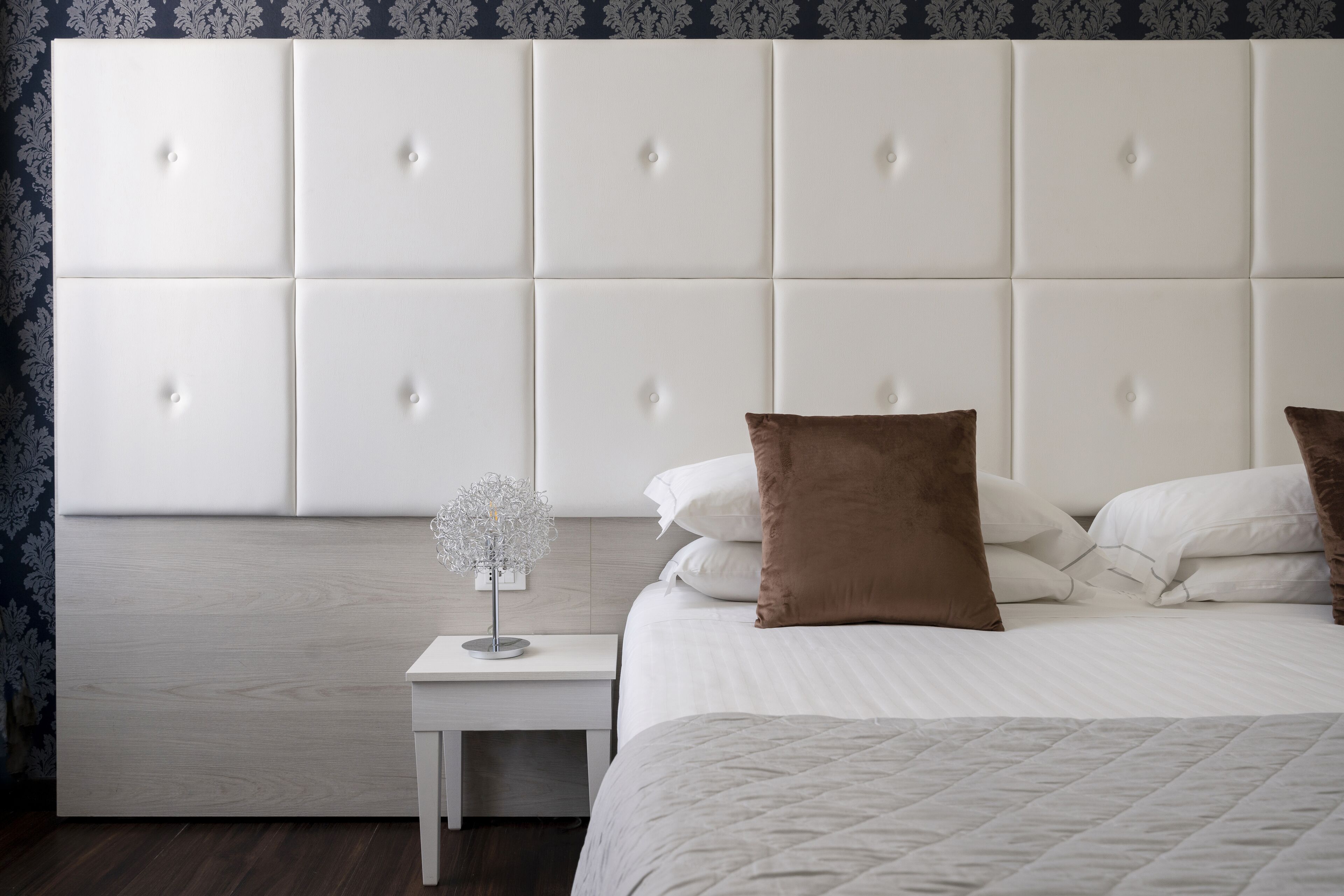A bedroom with a tufted headboard, a bedside table with a lamp, and a bed with pillows.