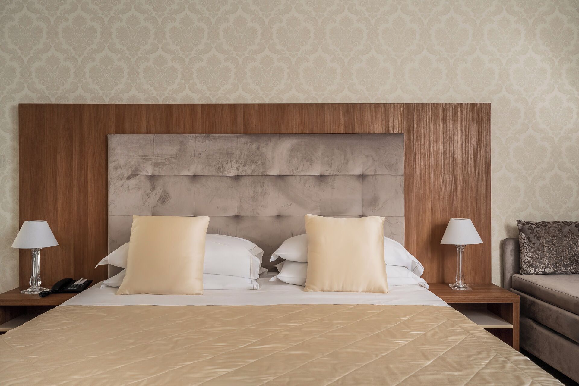 A hotel room with a large bed, two bedside tables with lamps, a telephone, and a small armchair.