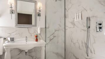 Un bagno con un lavabo in marmo, uno specchio con applique, una doccia con soffione estraibile e articoli da toilette a parete.