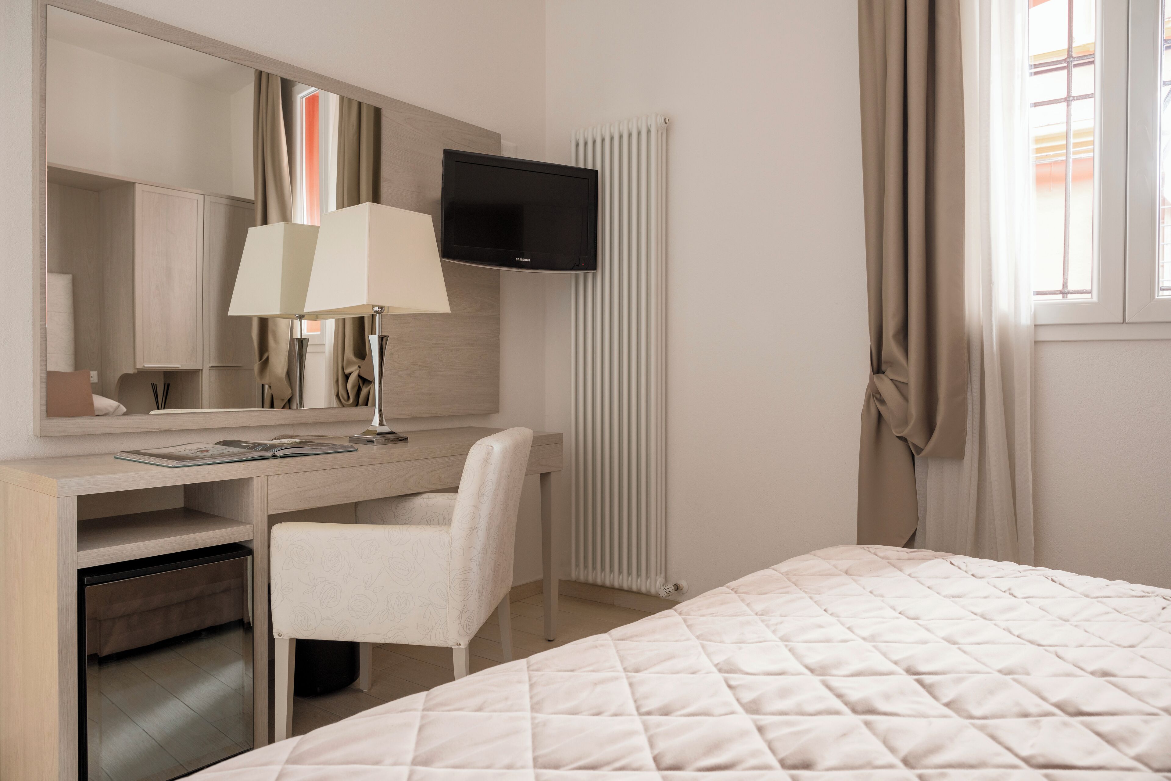 Een hotelkamer met een bed, een bureau met stoel, een televisie en een radiator.