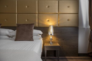 A neatly made bed with white linens and a brown pillow, a bedside table with a lamp, and a wooden headboard.