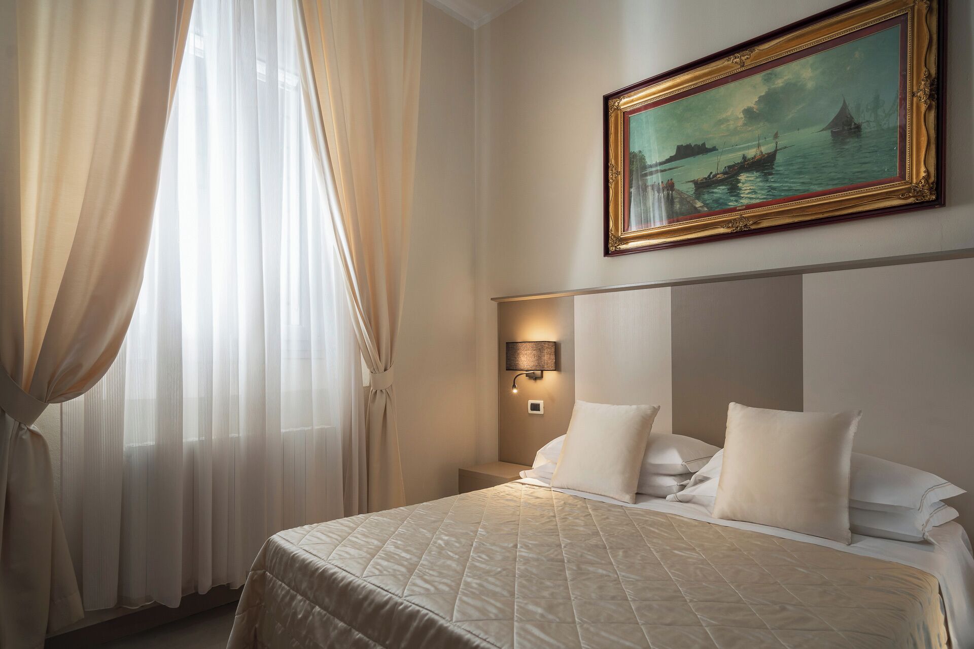 Una camera d'albergo con un letto, un comodino, una lampada e un quadro appeso al muro.