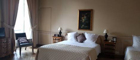 A hotel room with a bed, two bedside tables with lamps, a chair, a floral rug, and a painting on the wall.