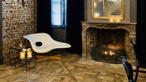 Une pièce aux murs en briques apparentes, dotée d’une cheminée moderne, d’un grand miroir et d’une chaise blanche originale.