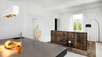 A modern kitchen with a large island, a stone sculpture, and a view of greenery outside.