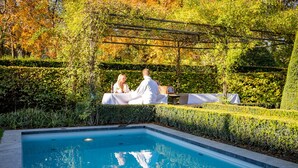 Un espace aménagé au bord de la piscine, avec une table pour deux, entouré d’une végétation luxuriante et agrémenté d’une pergola.