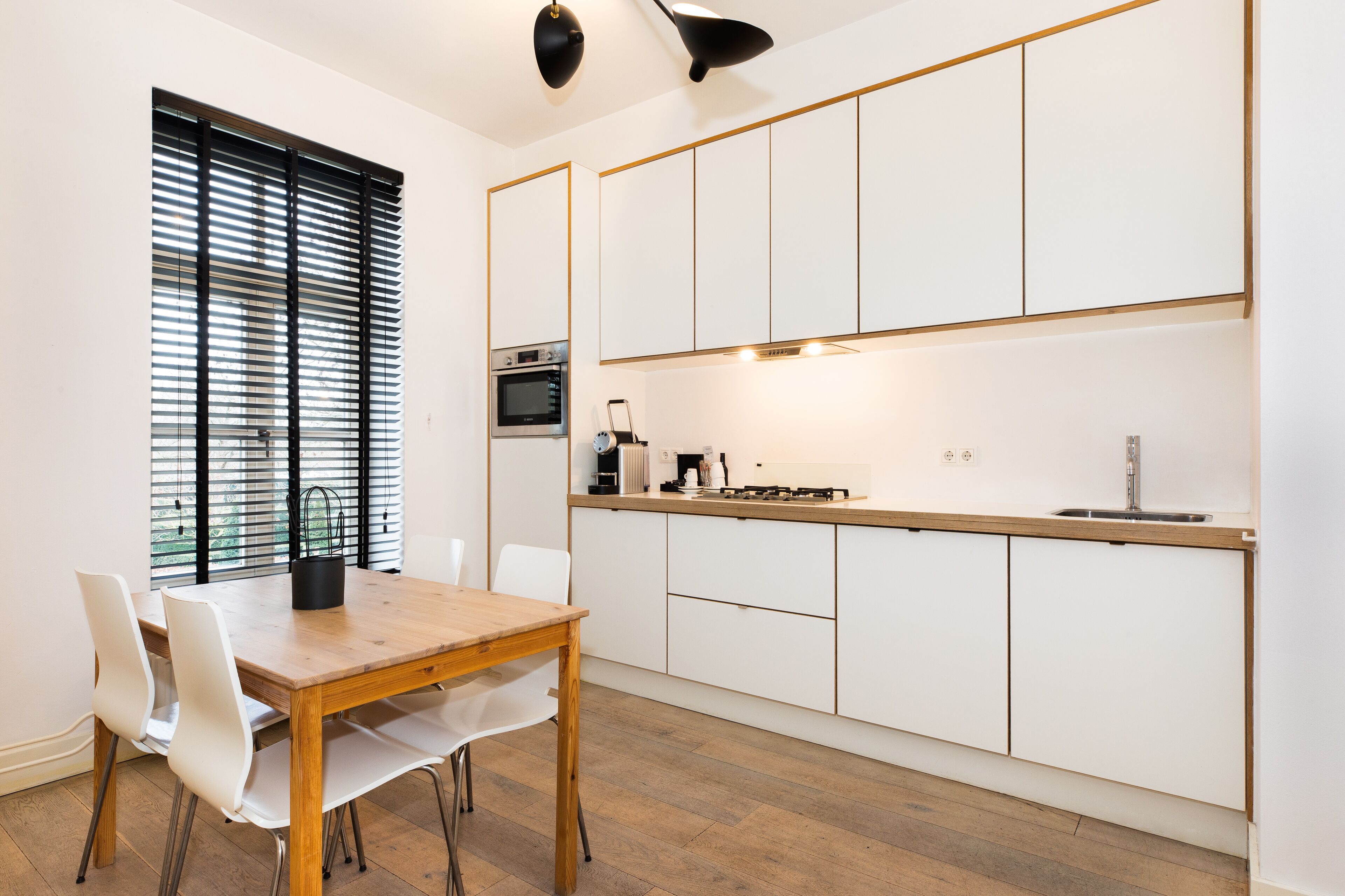 Een moderne keuken met witte kasten, een houten aanrecht en een eethoek met een houten tafel en witte stoelen.