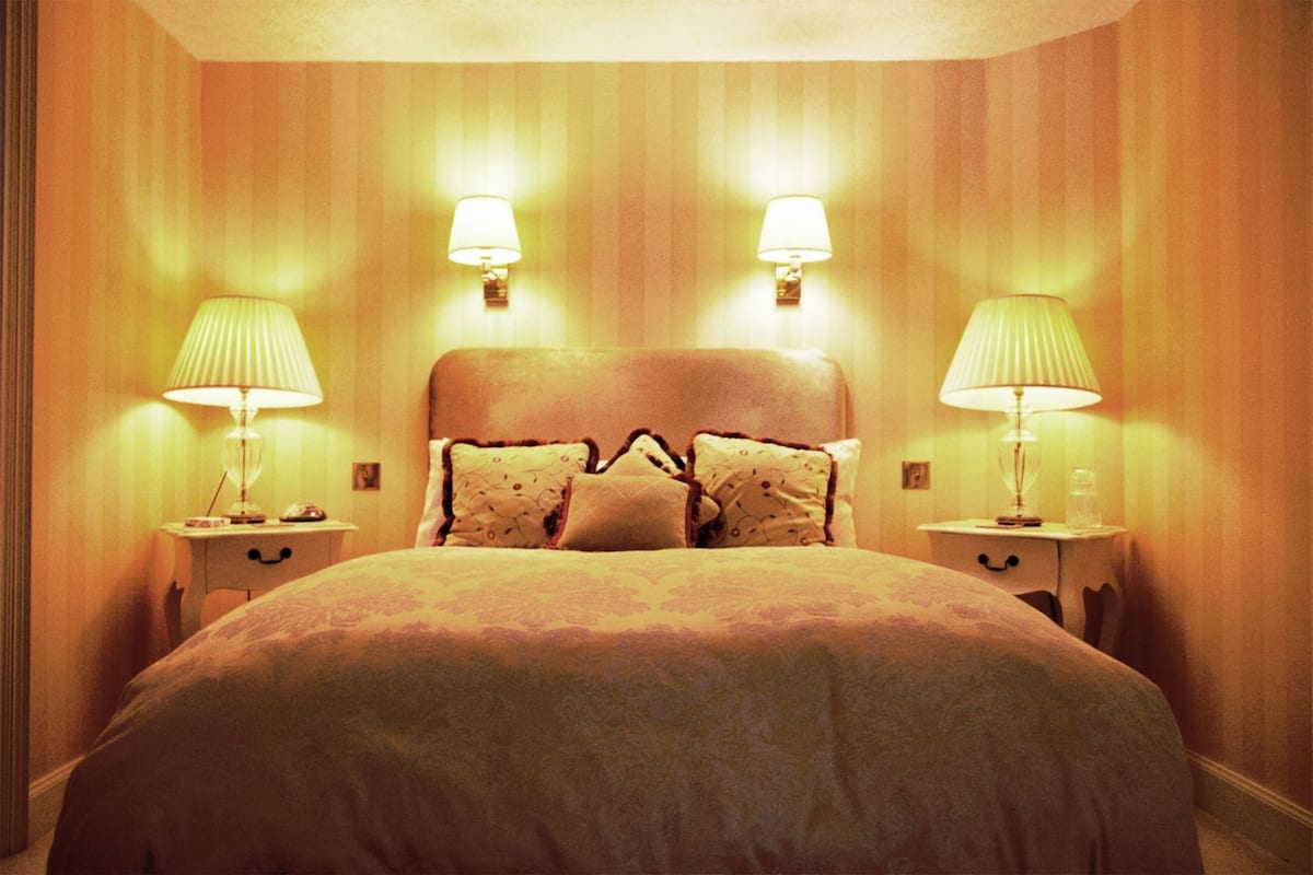 A hotel room with a large bed, two bedside tables with lamps, and a headboard with decorative pillows.