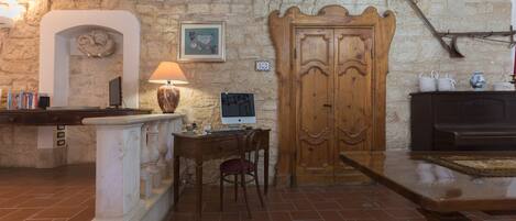 A rustic stone wall, a wooden door, a desk with a computer, a chair, and a fireplace.