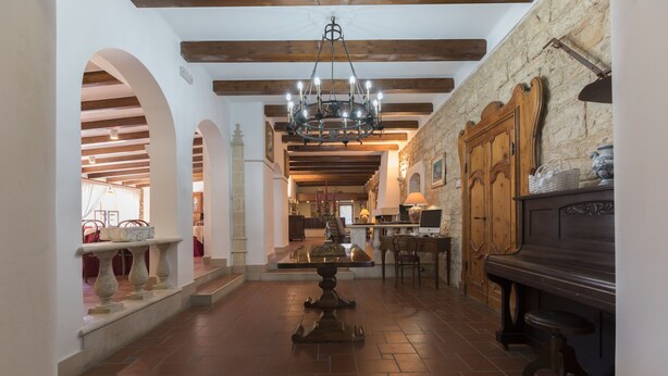 A spacious hall with a central table, wooden beams, stone walls, and a chandelier.