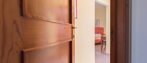 A wooden door with a handle, leading to a room with a bed and a chair.