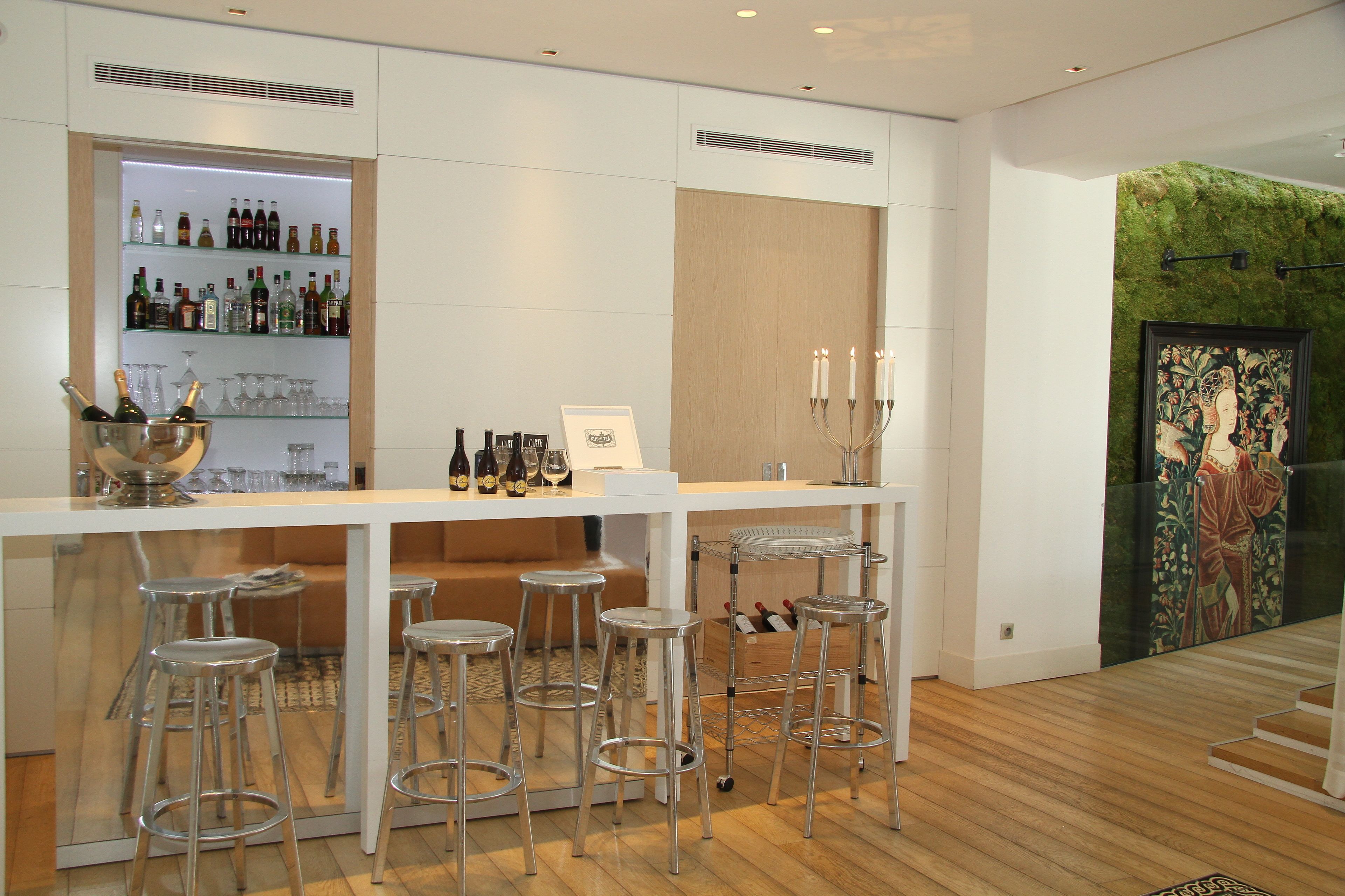 A bar area with a white countertop, multiple stools, and a wine bottle display.