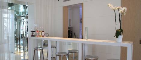 A modern kitchen with a white countertop, stainless steel stools, and a potted orchid.