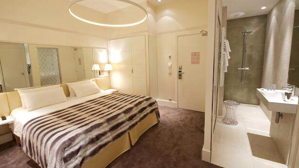 A hotel room with a large bed, a bathroom with a shower, and a mirror. - Le Cesar Hotel (Provins)