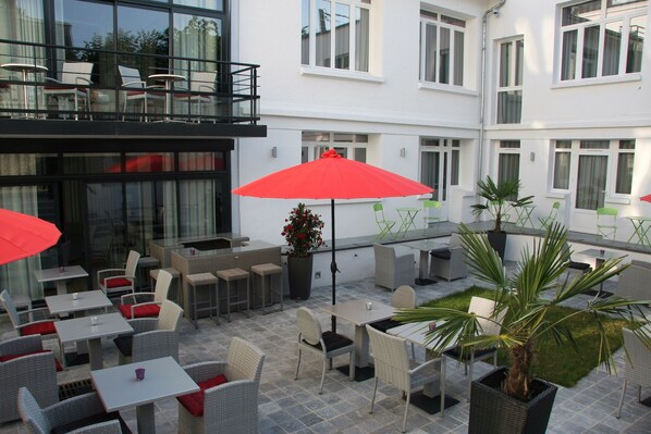 An outdoor patio area with tables and chairs, a red umbrella, and potted plants. - Le Cesar Hotel (Provins)