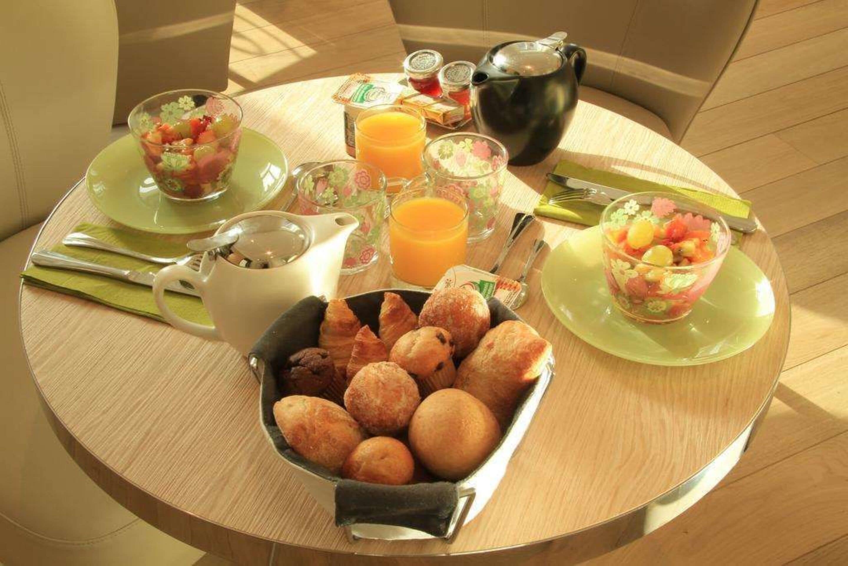 A breakfast table with a variety of food items including pastries, a fruit bowl, and orange juice.