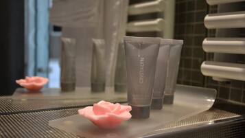 Une salle de bain avec un miroir reflétant les articles de toilette et un distributeur de savon rose en forme de rose.