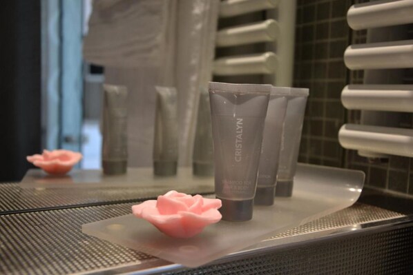 Une salle de bain avec un miroir reflétant les articles de toilette et un distributeur de savon rose en forme de rose.