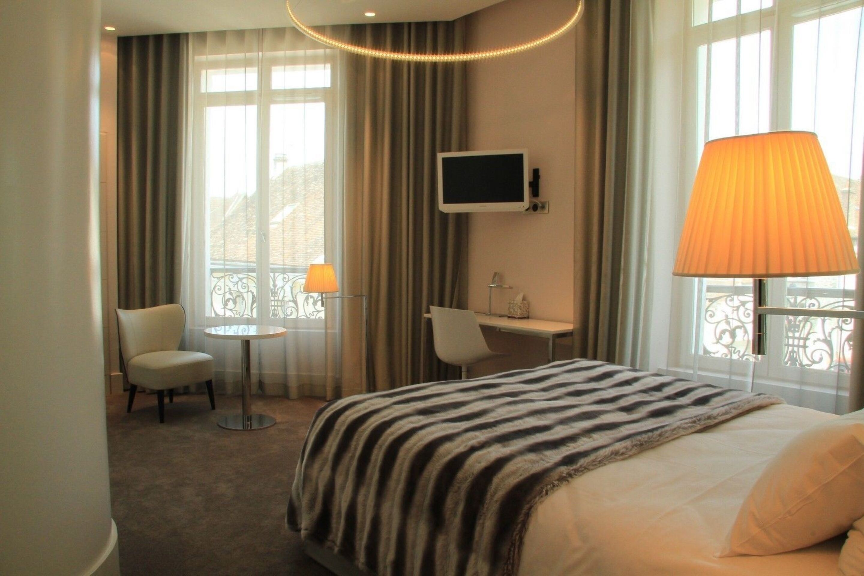 Habitación de hotel con cama, escritorio, silla, televisor y lámpara.