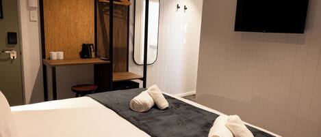 Habitación de hotel con cama, toalla negra, estante de madera, espejo y televisor de pantalla plana.