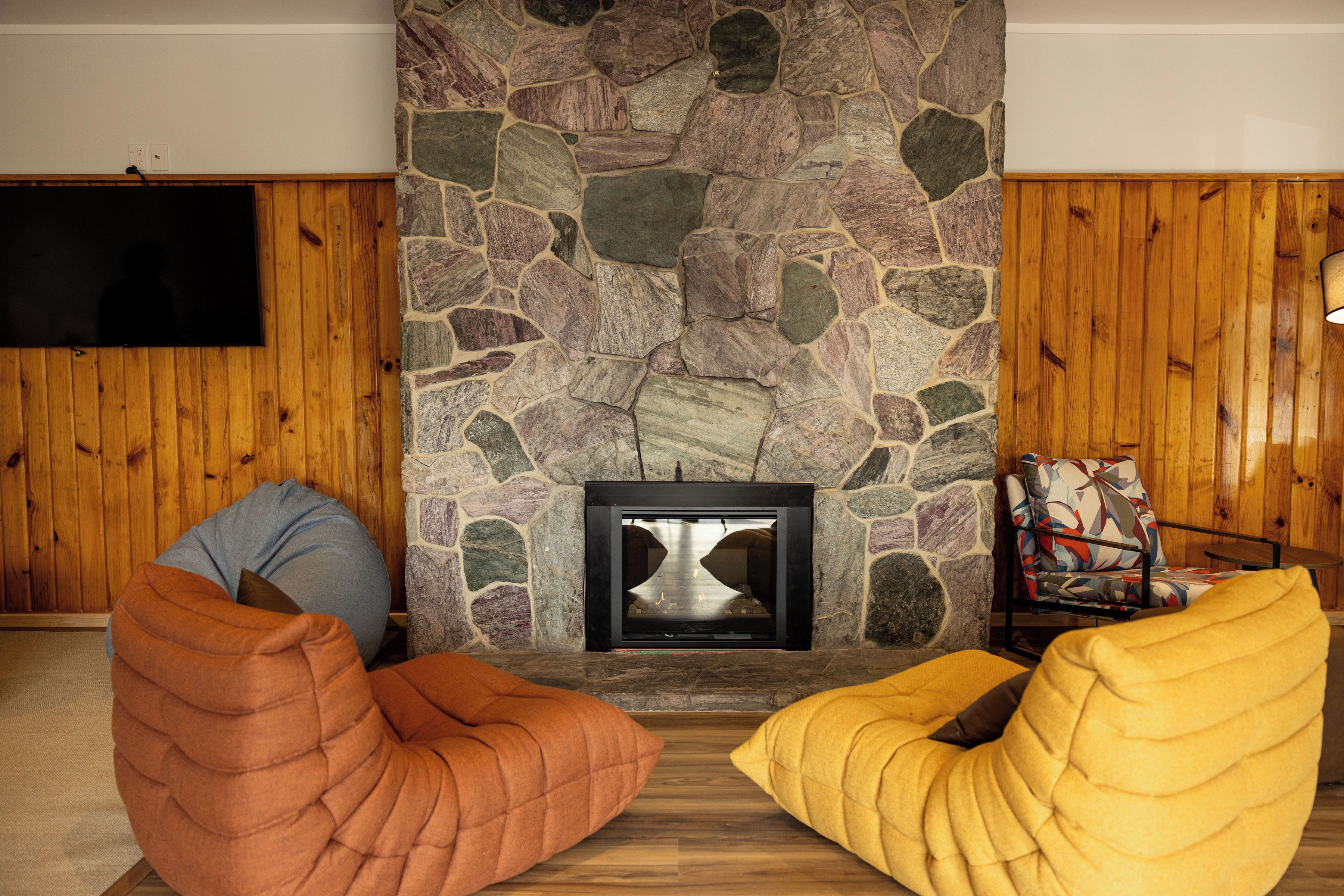 Een kamer met een stenen openhaard, houten wanden en twee loungestoelen.