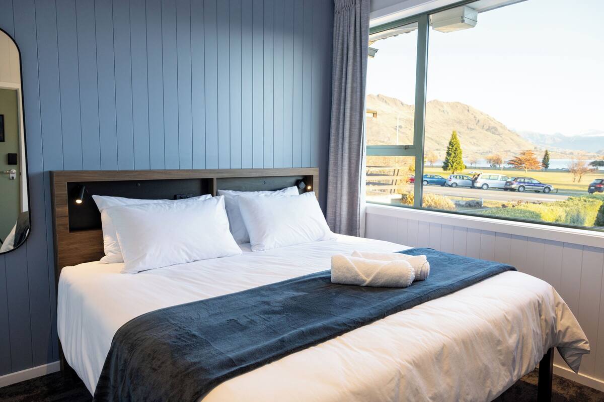 A hotel room with a large bed, a view of the parking area, and a mountain in the background.
