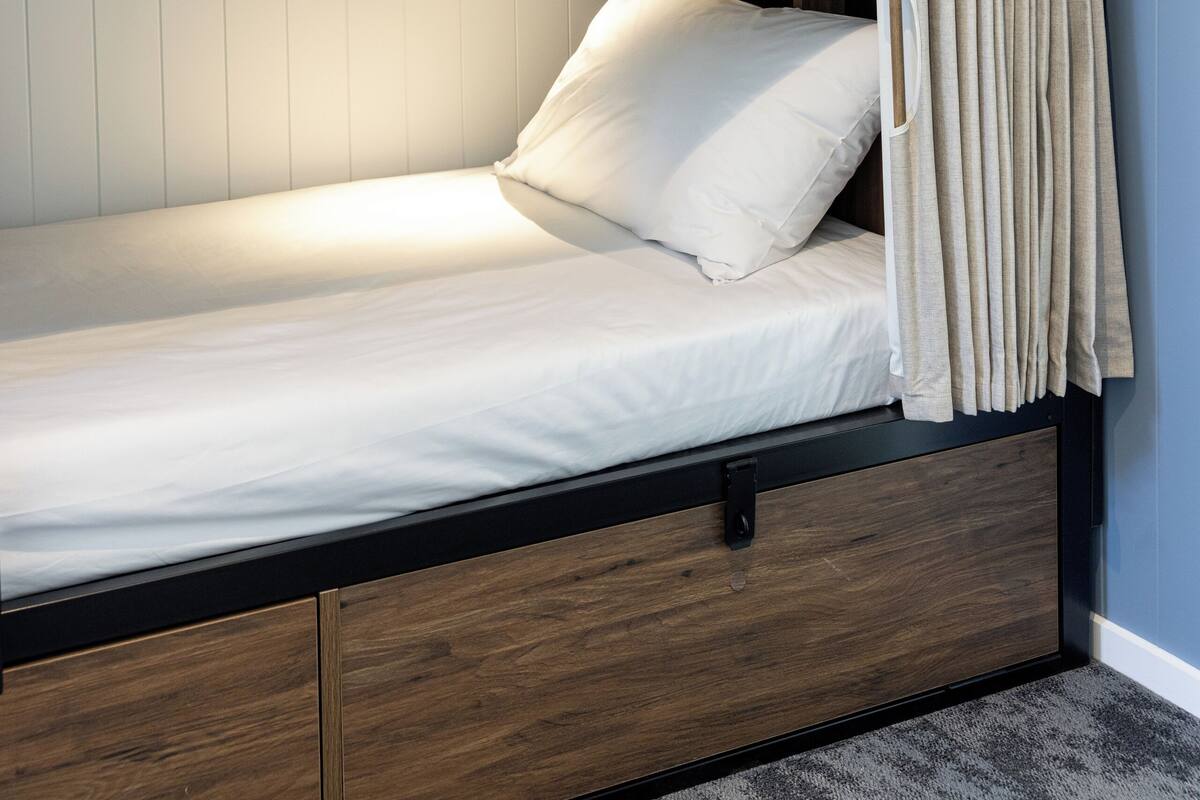 A bunk bed with a wooden frame, a white mattress, and a curtain.