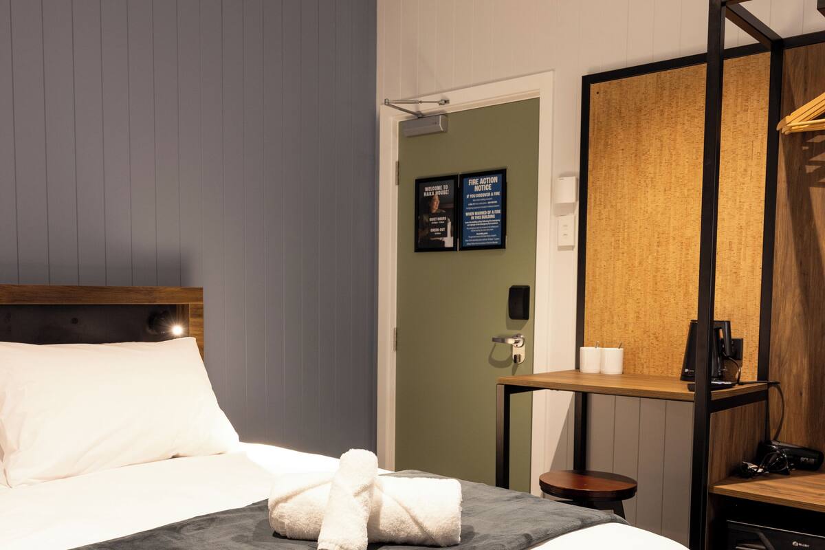 A hotel room with a bed, a small table, a chair, a mirror, and a door.