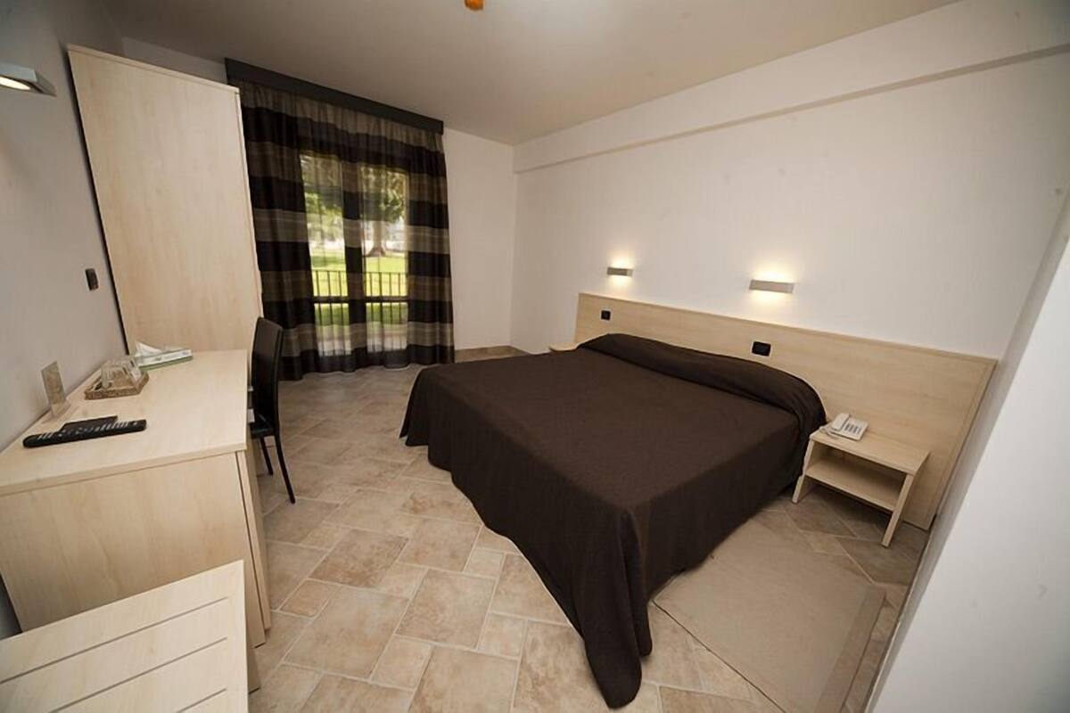 Ein Schlafzimmer mit Bett, Schreibtisch, Stuhl, Nachttisch und einem Fenster mit Vorhängen.