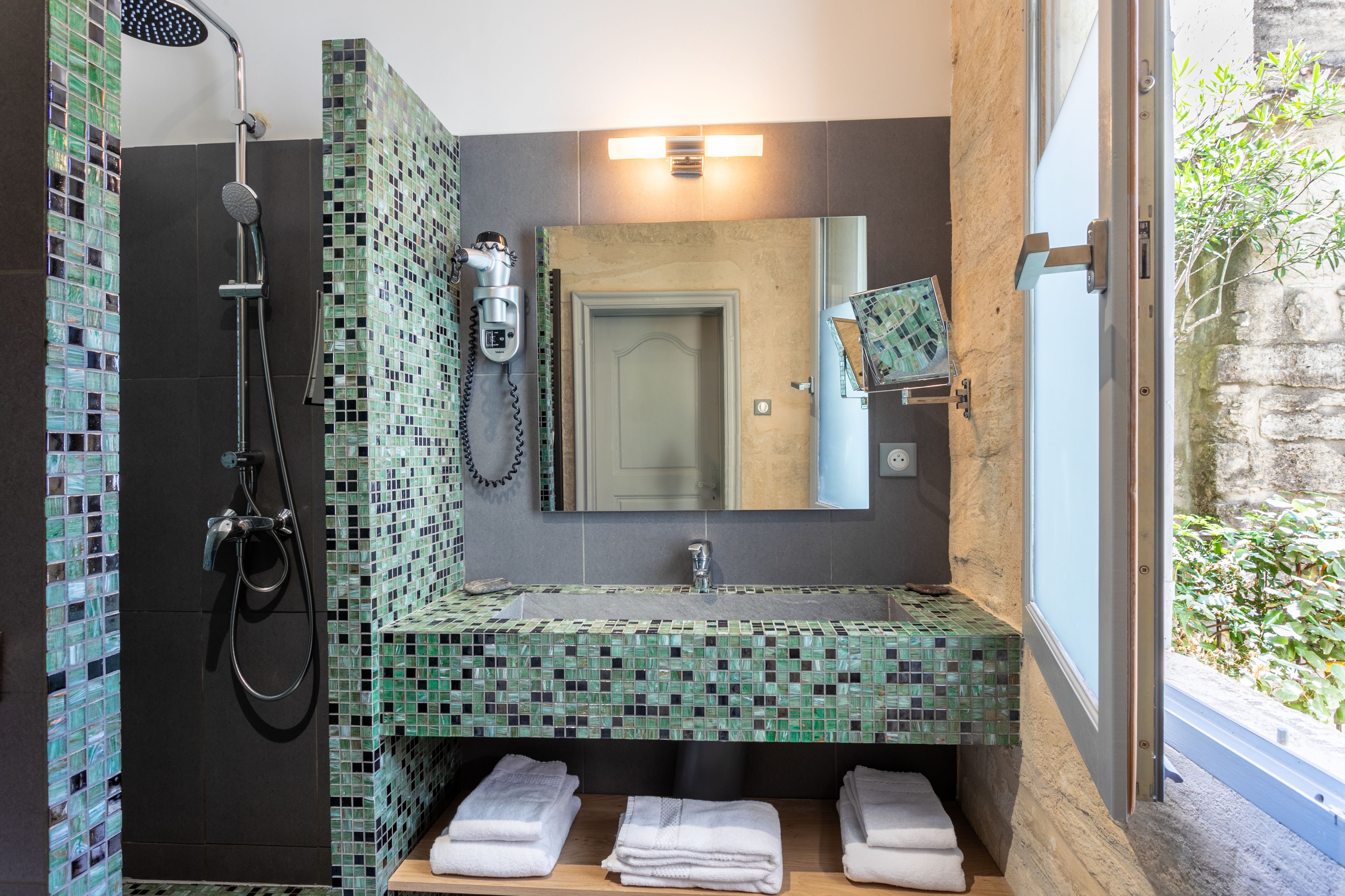 Un bagno con doccia in mosaico, un lavandino con specchio e asciugamani su uno scaffale.