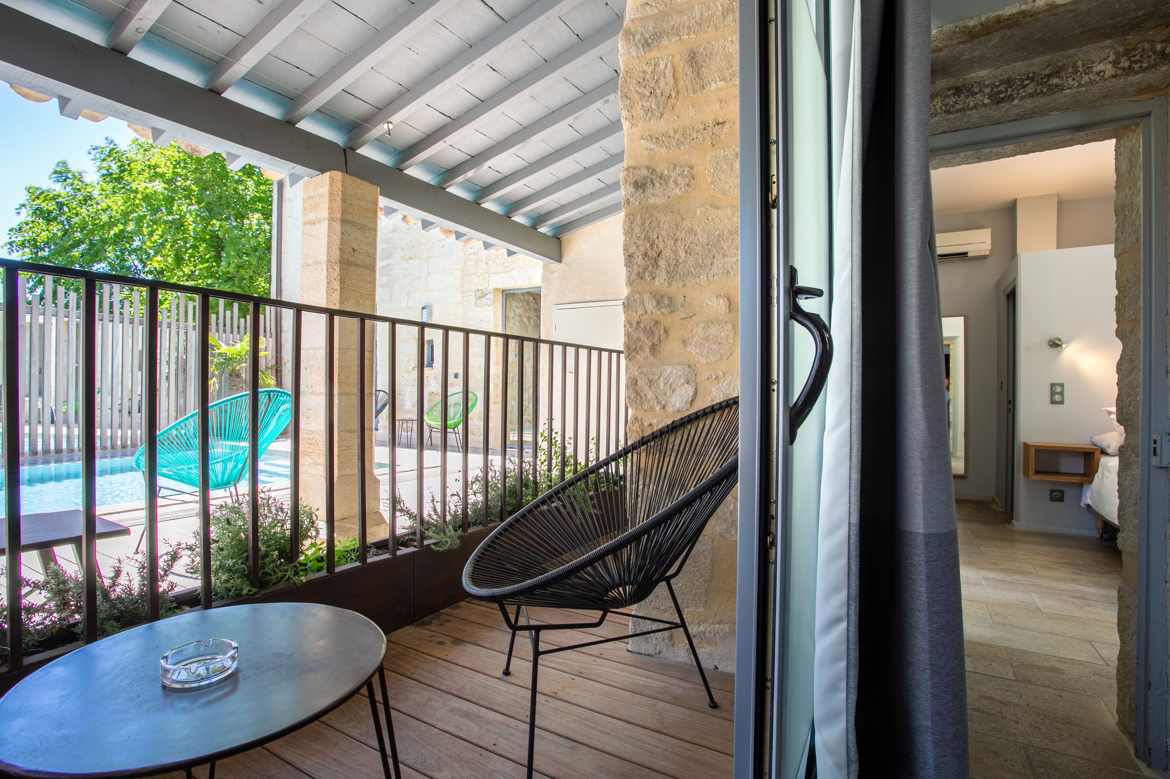 Un balcón con una mesa y una silla, una piscina y un muro de piedra.