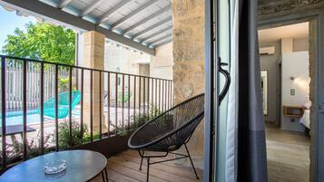 Un balcón con una mesa y una silla, una piscina y un muro de piedra.