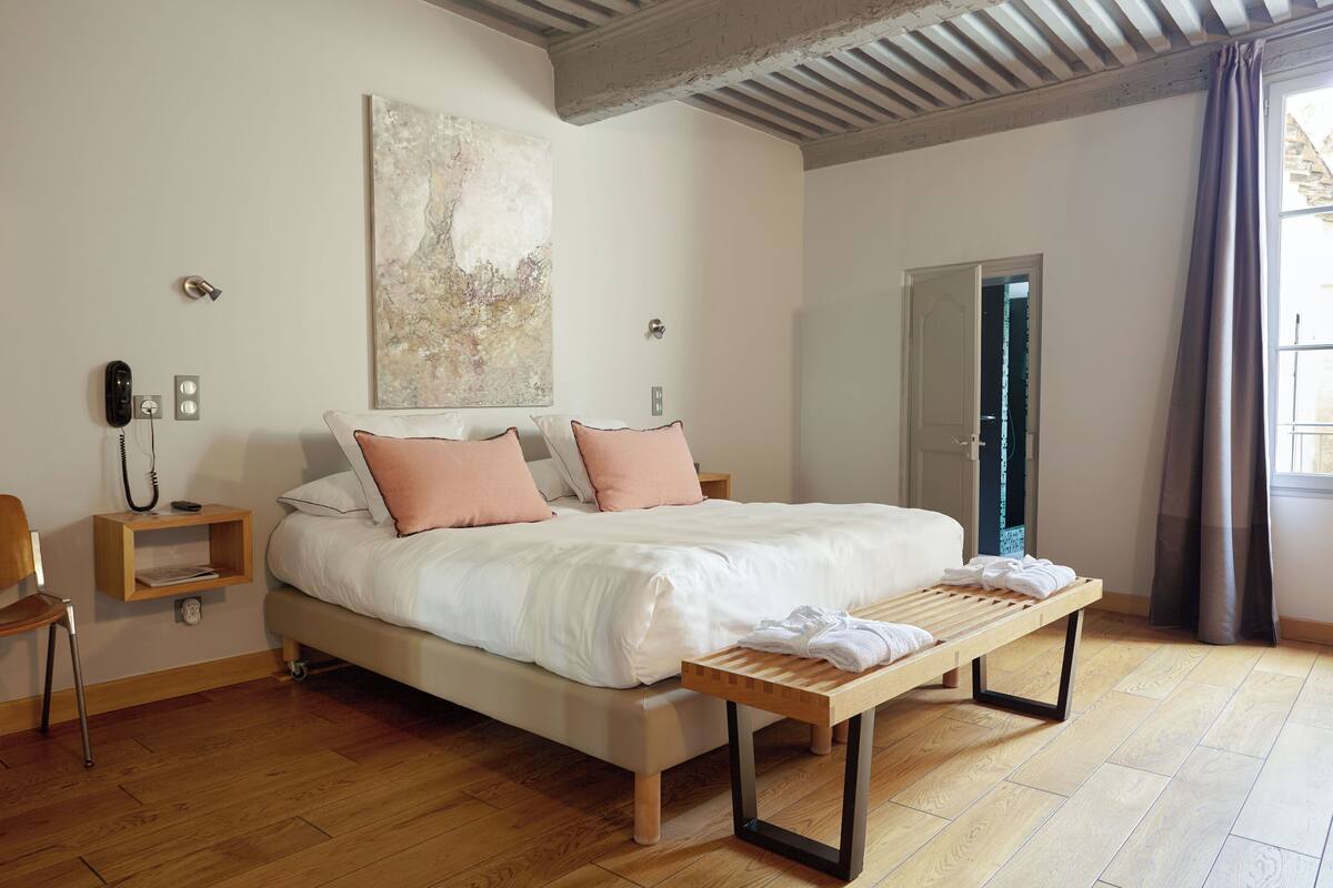A modern bedroom with a large bed, bedside tables, a wooden bench, and a large abstract painting on the wall.