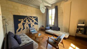 Een woonkamer met een bank, fauteuils, een salontafel, een schilderij en een open haard.
