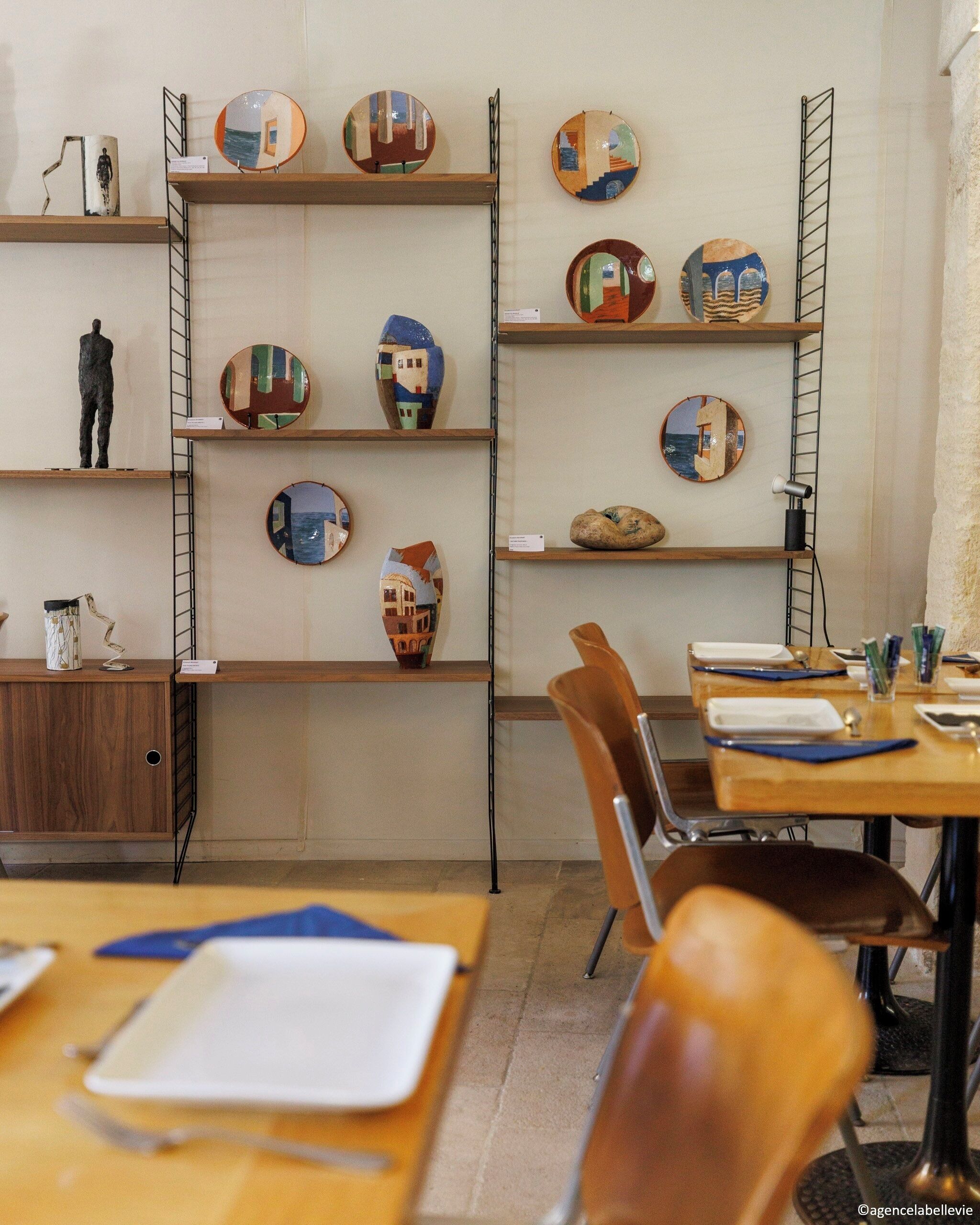 Habitación con estanterías de madera que muestran diferentes platos de cerámica, una pequeña estatua y un escritorio con una silla.