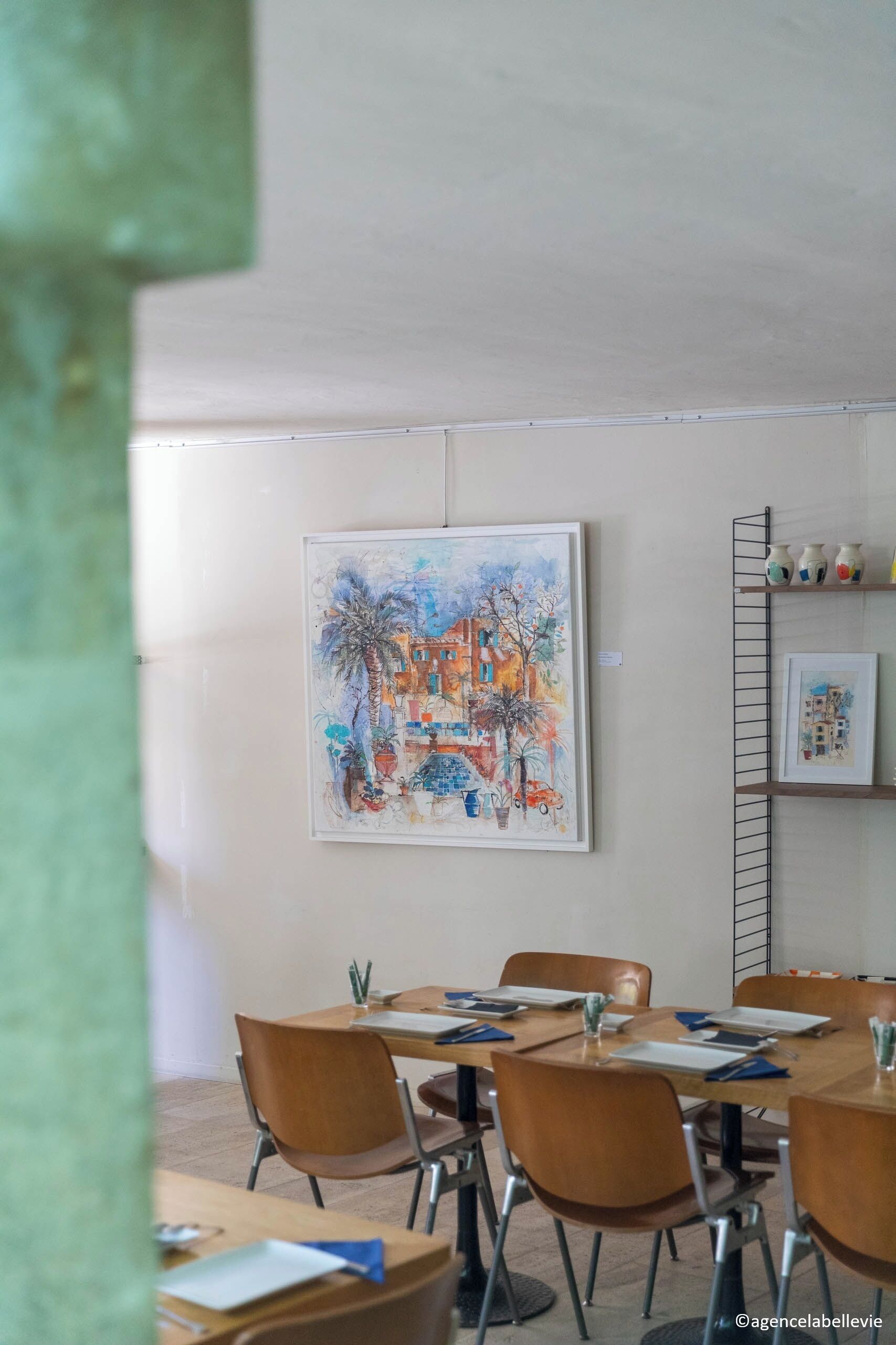 Un comedor con mesas y sillas, un cuadro en la pared y un estante con adornos.
