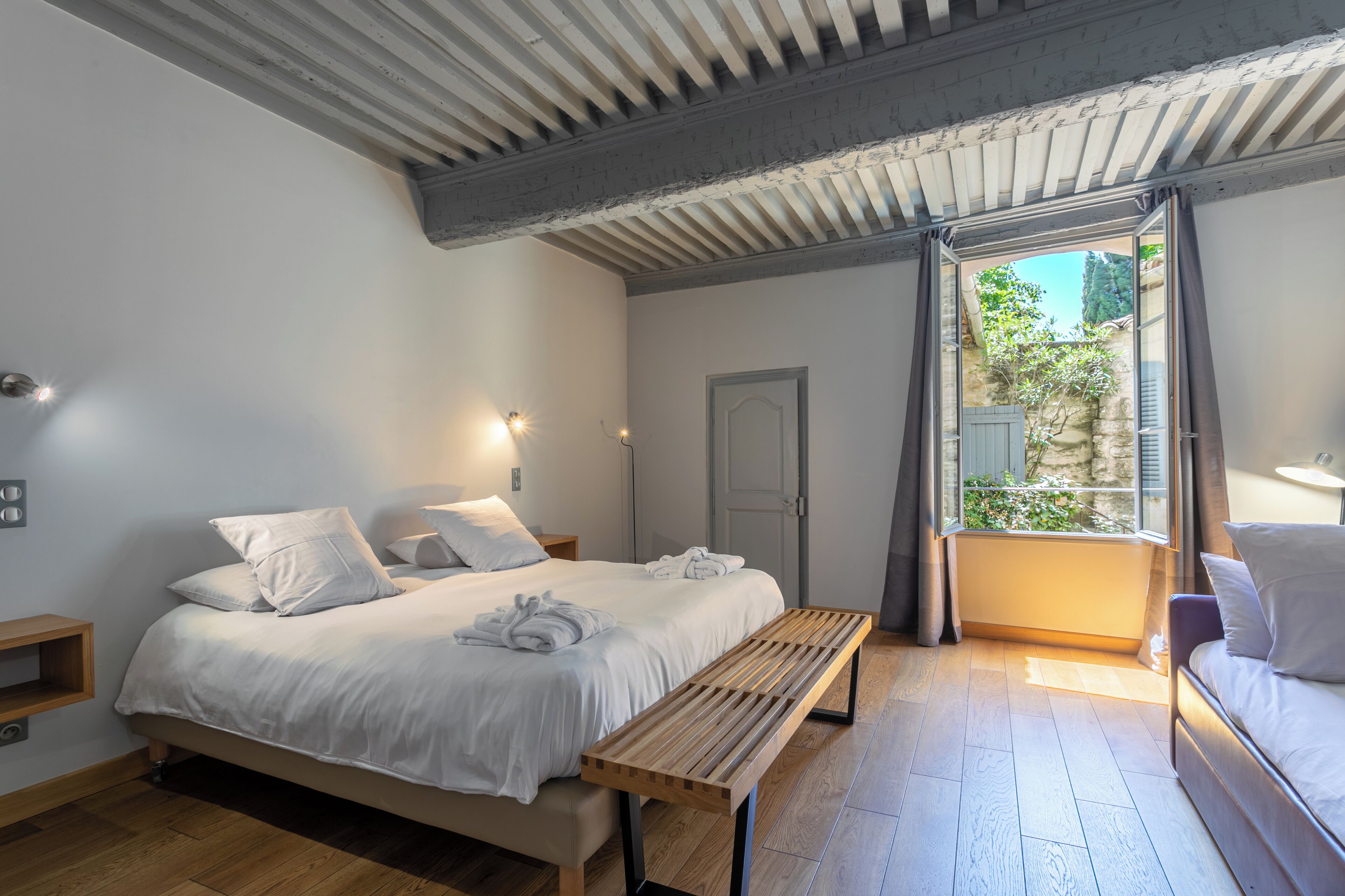 A bedroom with a bed, bedside tables, a bench, a door, and a window with curtains.