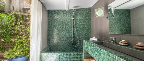 A bathroom with green mosaic tiles, a shower, a sink with a mirror, and a potted plant.
