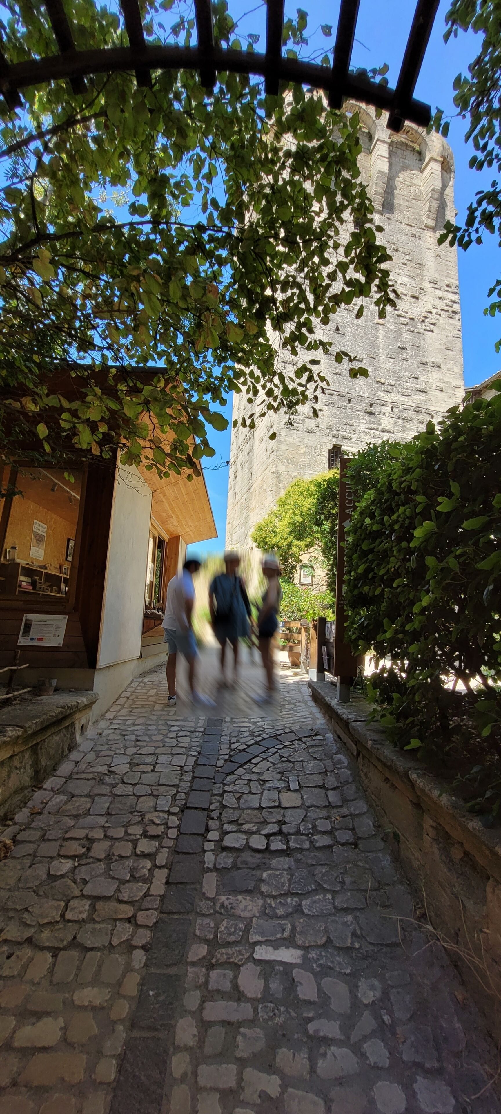 A cobblestone street leading to a historic stone building with a wooden structure on the left.