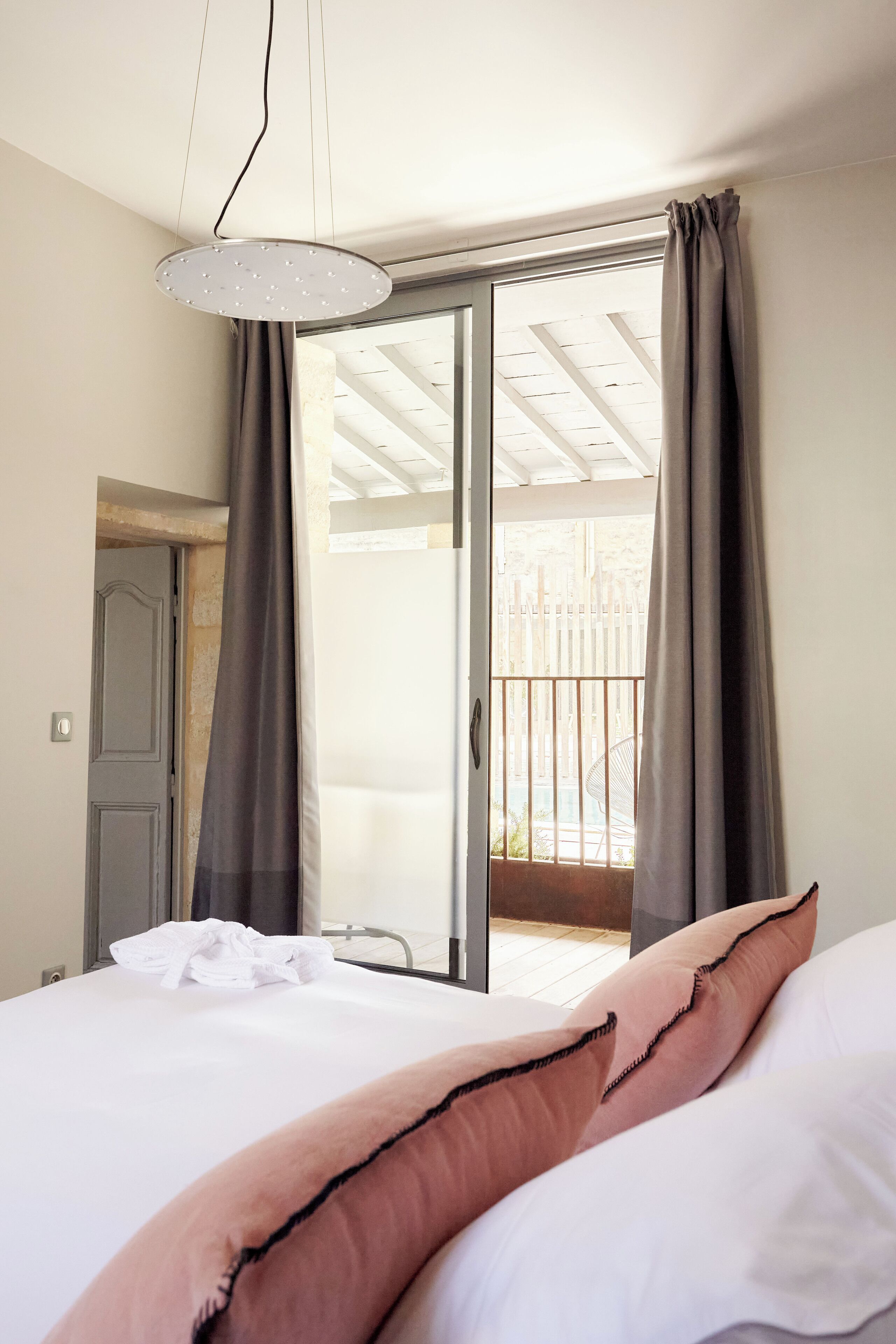 Un dormitorio con cama, ventana con cortinas, luz de techo y vista al balcón exterior.