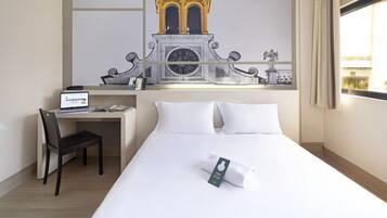 A hotel room with a bed, a desk, a chair, and a large window.