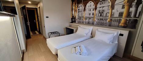 Habitación de hotel con dos camas, un escritorio y un mural de un edificio con arcos.